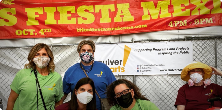 People in facemasks standing in front of Titos Fiesta banner